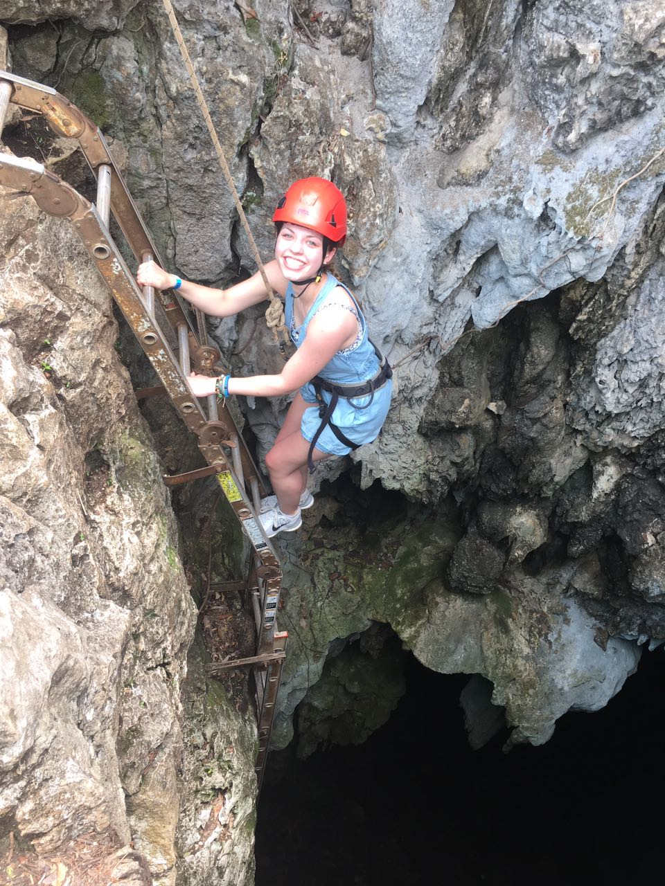 Traveler with red helmet descending a ladder into the Venado limestone caves in Costa Rica